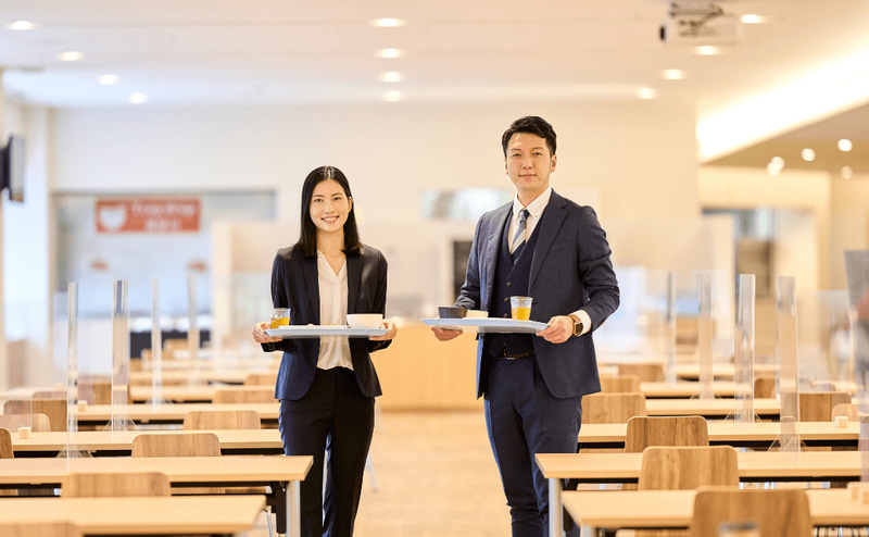 食堂でお盆を持つ社員（男女）